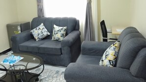 A living room with two grey sofas, a glass coffee table, and a small side table. - Oltotoi suites (Kitengela)