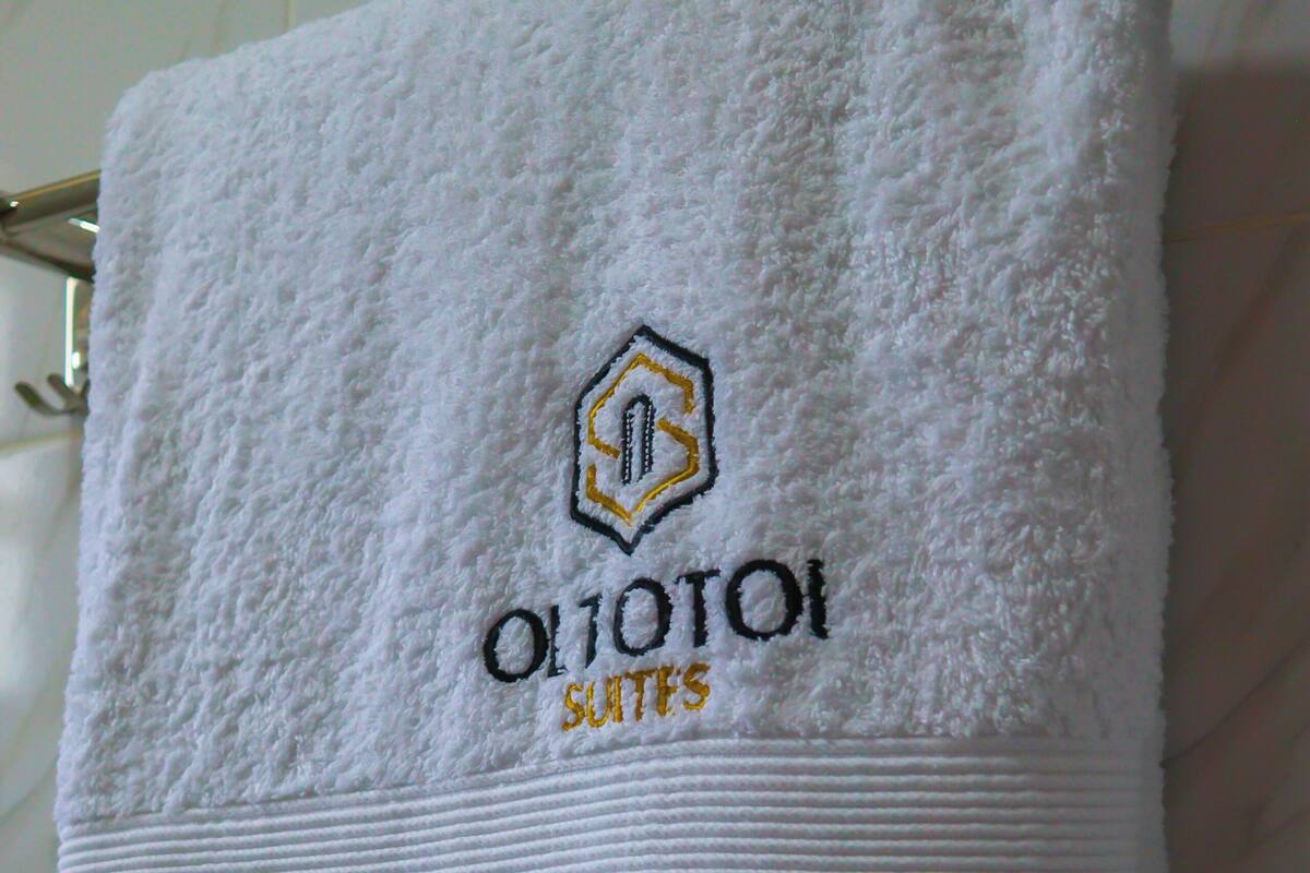 A white towel with embroidered text and a logo, hanging on a metal towel rack.