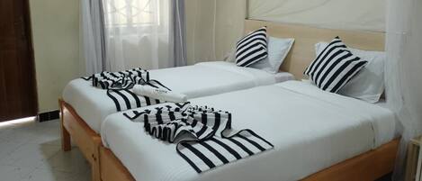 Una habitación con dos camas, cada una con ropa blanca y almohadas a rayas.