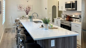 Cozinha moderna com ilha central, banquetas, eletrodomésticos de aço inoxidável e iluminação pendente.