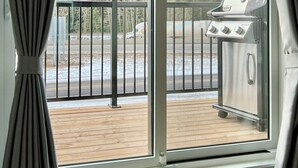 Uma varanda com vista para montanhas nevadas, uma churrasqueira e um deck de madeira.