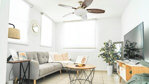 A modern living room with a grey sofa, a round coffee table, a ceiling fan, a TV, and a potted plant. - Boho Style with Private Pool, Cozy 3-bedroom house in beautiful Guayama WiFi, AC (Guayama)