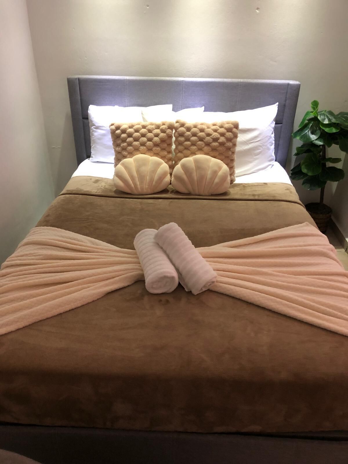 Cama bem arrumada com cobertura marrom, duas almofadas e arranjo decorativo de toalhas.