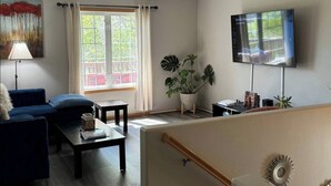 Olohuoneessa on sohva, sohvapöytä, televisio ja suuri ikkuna, jossa on verhot.