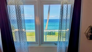 A room with a wooden floor, a window with a view of the beach, and a curtain. - Modern Oceanfront Apartment  (Arecibo)