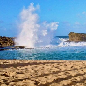A beach with waves crashing against rocks and a clear sky. - Modern Oceanfront Apartment  (Arecibo)