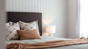 Una cama bien hecha con una manta marrón, un cabecero gris y almohadas estampadas.