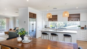 Una cocina moderna con armarios blancos, una isla central con taburetes y luminarias colgantes.