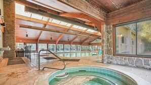 Une piscine intérieure avec un mur en pierre et des poutres en bois, entourée de chaises longues et dotée d’une grande fenêtre.
