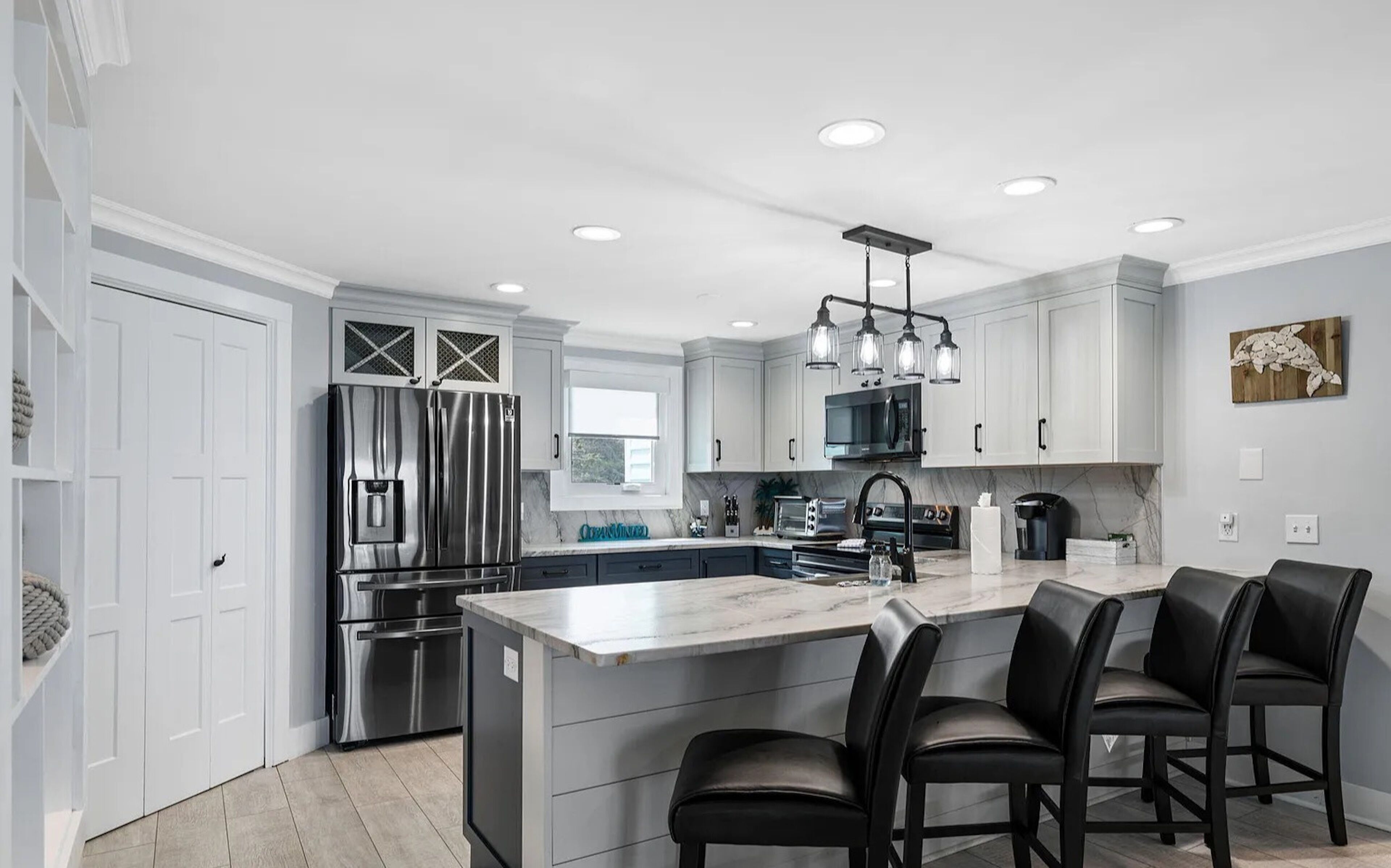 A modern kitchen with a central island, stainless steel appliances, and a bar area with black leather chairs.