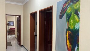 A hallway with a tiled floor, wooden doors, and a large abstract painting on the wall.