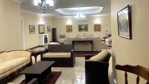 A spacious living room with a fireplace, multiple seating options including sofas and chairs, a dining table, and a chandelier.