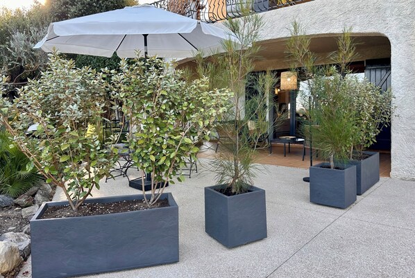 Un patio con plantas en macetas, mobiliario exterior y un gran paraguas.