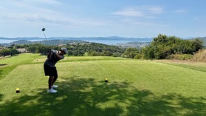Un parcours de golf offrant une vue dégagée sur le paysage environnant, notamment sur les collines lointaines et une étendue d’eau.
