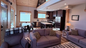 A spacious living area with a high ceiling, wooden beams, a dining area, and a kitchen.