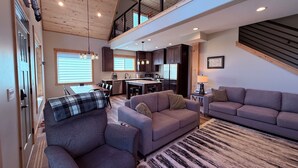 A spacious living area with a high ceiling, wooden beams, and a modern kitchen in the background.