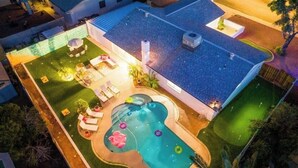 Ett flygbildsfoto av en bostadsfastighet med en swimmingpool, ett utomhusområde med sittplatser och en täckt uteplats.