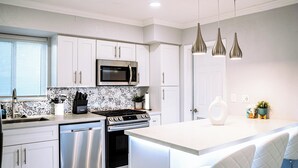 Una cocina moderna con armarios blancos, electrodomésticos de acero inoxidable, un salpicadero estampado e iluminación colgante.