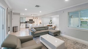 Una sala de estar moderna con un sofá modular, una mesa de centro blanca y una cocina al fondo.
