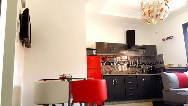 A compact kitchen with modern appliances, a dining area with a red chair, and a living space with a sofa and a red rug. - ⭐ Charming Apartment in Marrakech (Marrakech)