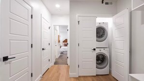 A laundry room with two washing machines, a hallway with white doors, and a bedroom in the background. - Powder Mountain Ski Retreat, an art-inspired townhome in the heart of Eden (Eden)