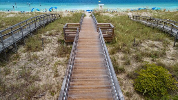 A wooden boardwalk leading to a beach with clear blue water and a lifeguard tower in the distance. - The Turquoise Turtle -Private Pool, Hot Tub, Ocean View, 2nd Row, 4BR, Kids Area (Carolina Beach)