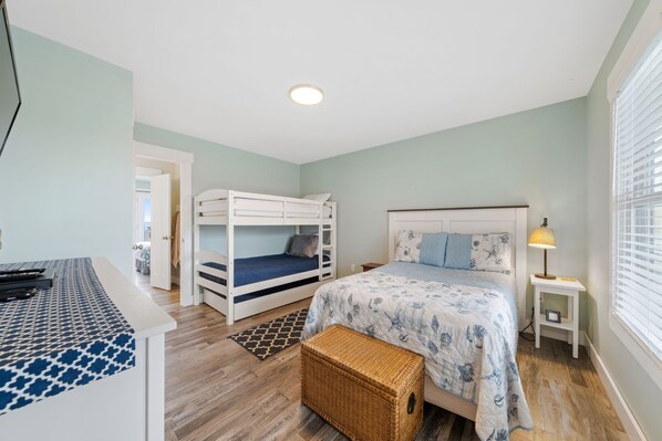 A bedroom with a bunk bed, a single bed, a bedside table with a lamp, and a wicker basket.