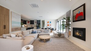En moderne stue med en hjørnesofa, et rundt sofabord og en pejs. I baggrunden er der et spiseområde med et køkken.
