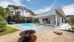 Et moderne hus med swimmingpool, udendørs møbler og bålsted.