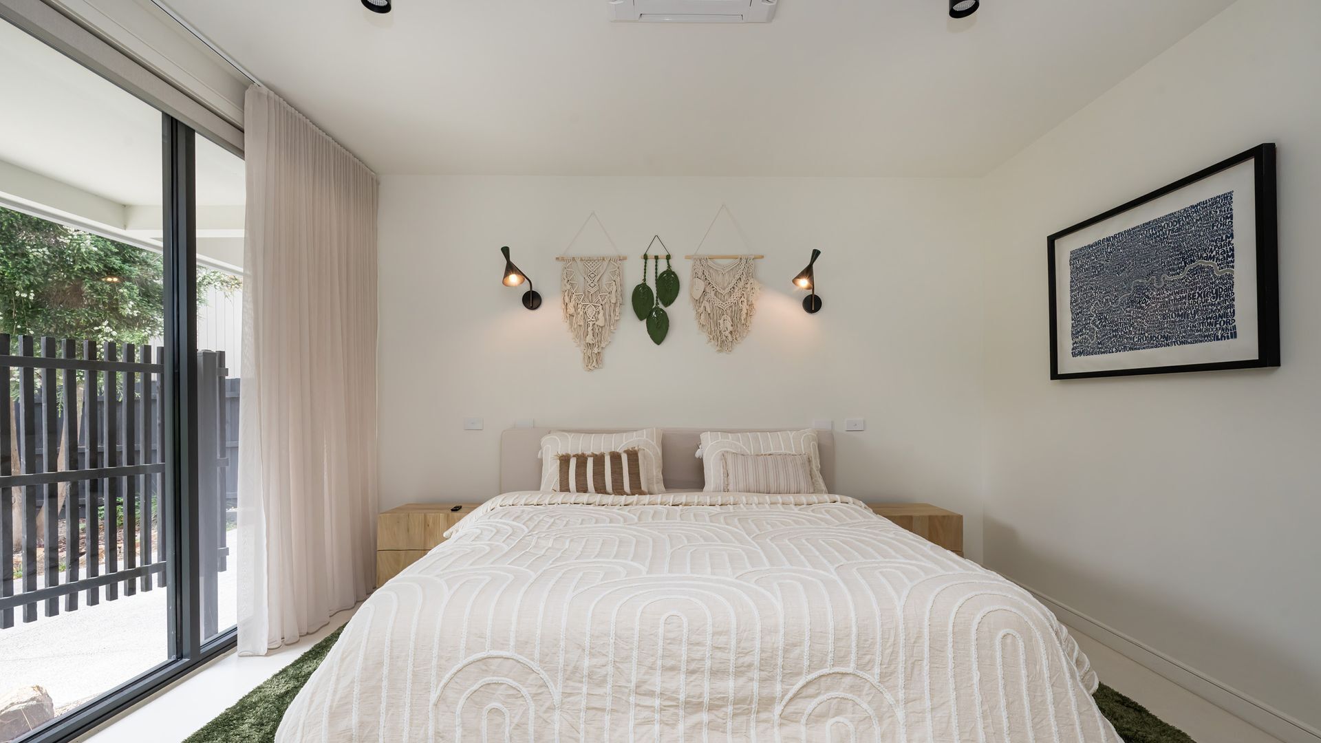 A bedroom with a large bed, a window with a view of the outdoors, and a wall-mounted macrame decoration.