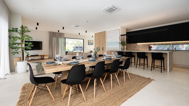 A modern dining area with a long wooden table set for six, surrounded by black chairs.