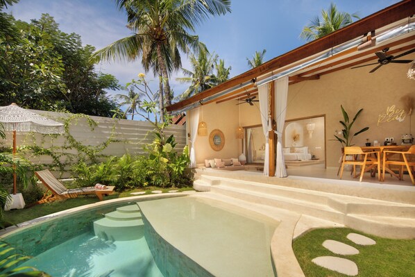 A poolside area with a lounge chair, a dining table with chairs, and a staircase leading to a covered patio.