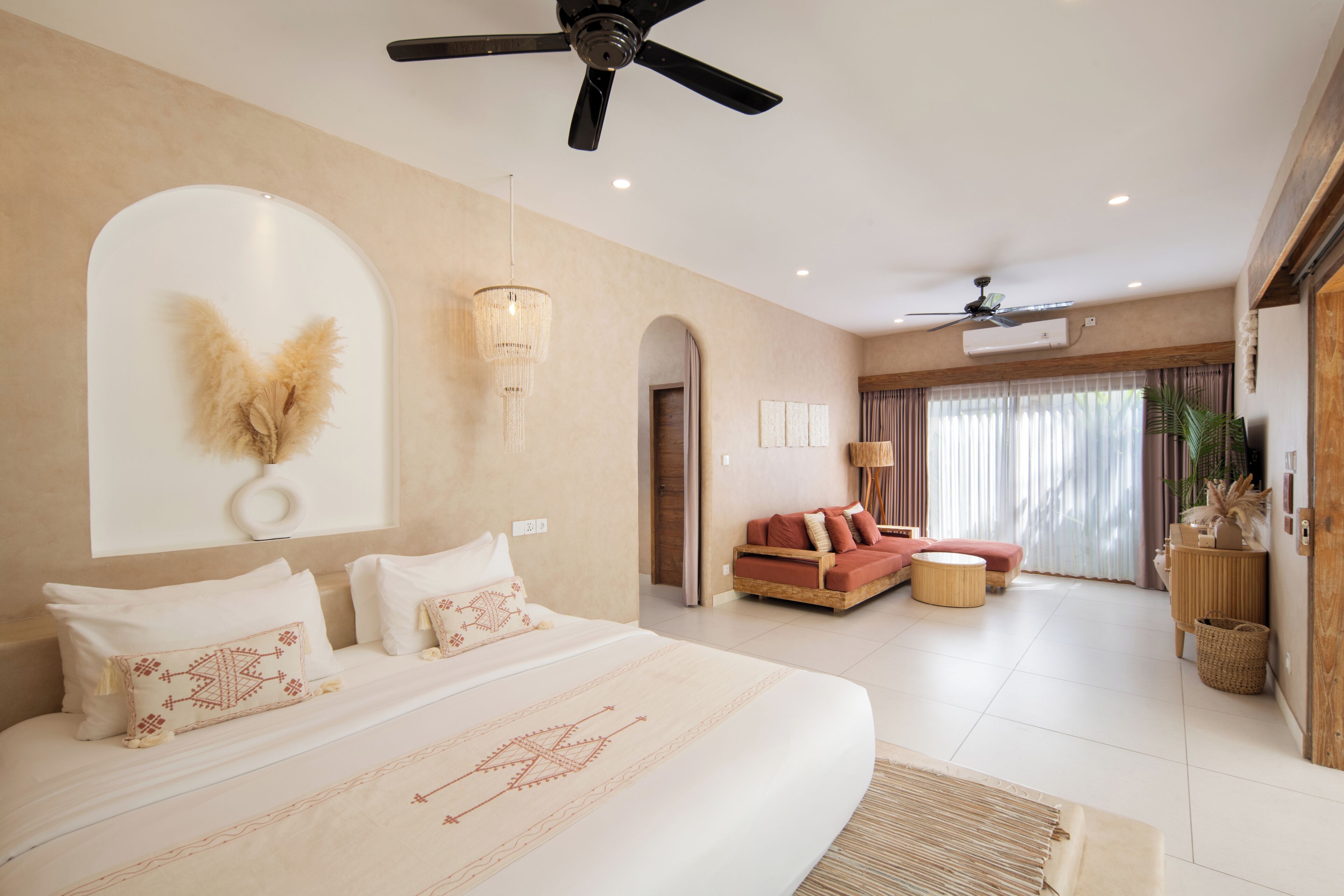 A spacious bedroom with a large bed, a ceiling fan, an air conditioning unit, and a seating area with a sofa and a small table.