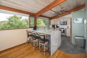Una cocina moderna con una isla grande, taburetes de bar y vistas a árboles a través de las ventanas.