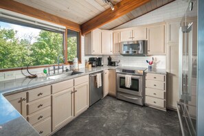 A modern kitchen with a large window, stainless steel appliances, and light wood cabinetry.