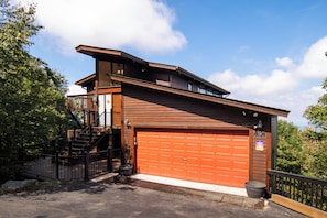 A two-story building with a red garage door, a balcony, and a staircase leading to the upper level. - Pet-Friendly 5BR Home! Spectacular Mtn Views, Hot Tub, 5 min to Beech Ski (Beech Mountain)