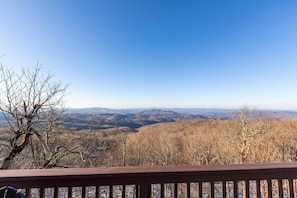 Une vue depuis une terrasse en bois, donnant sur un paysage montagneux sous un ciel dégagé.