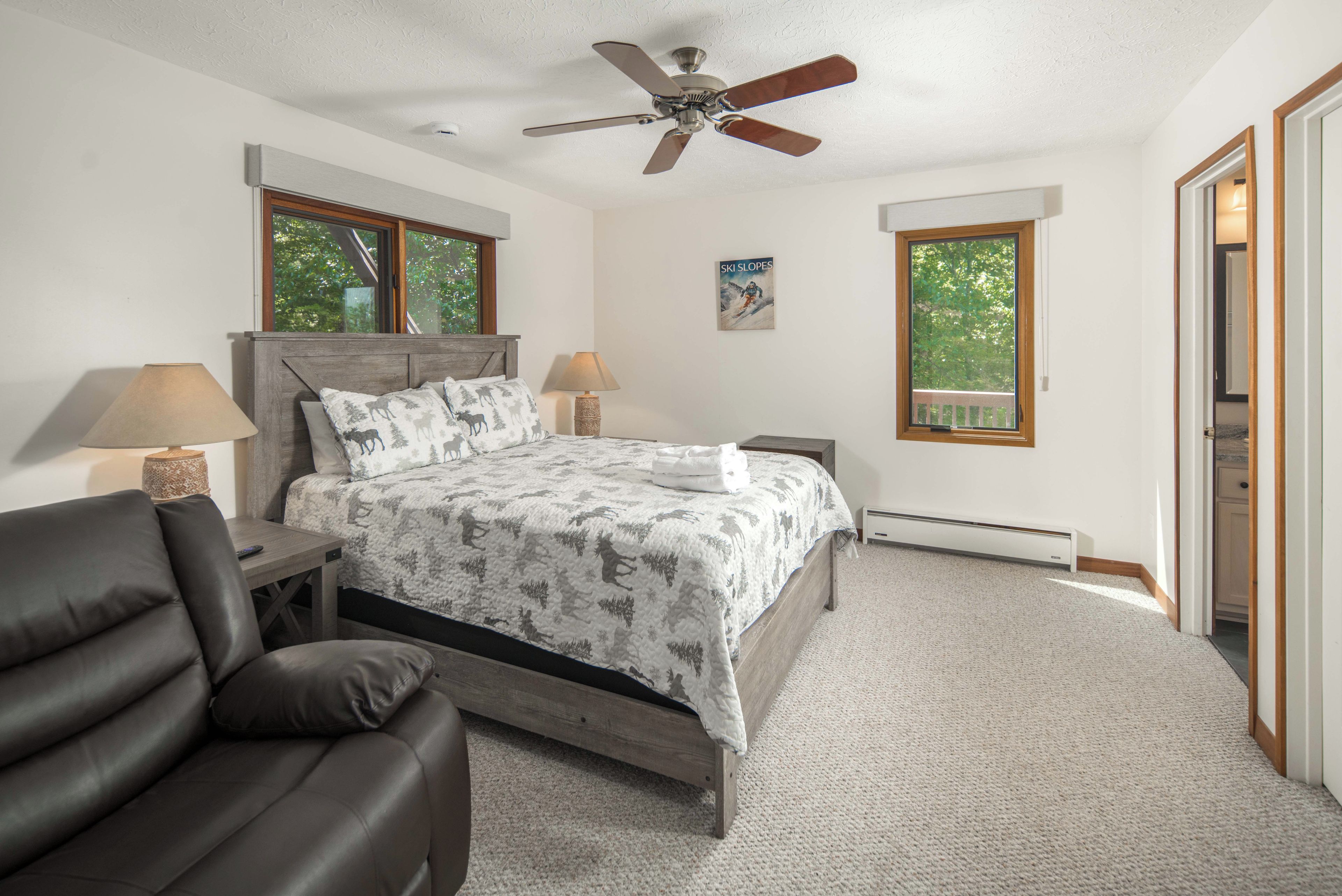 A bedroom with a bed, two bedside tables, a ceiling fan, and two windows.
