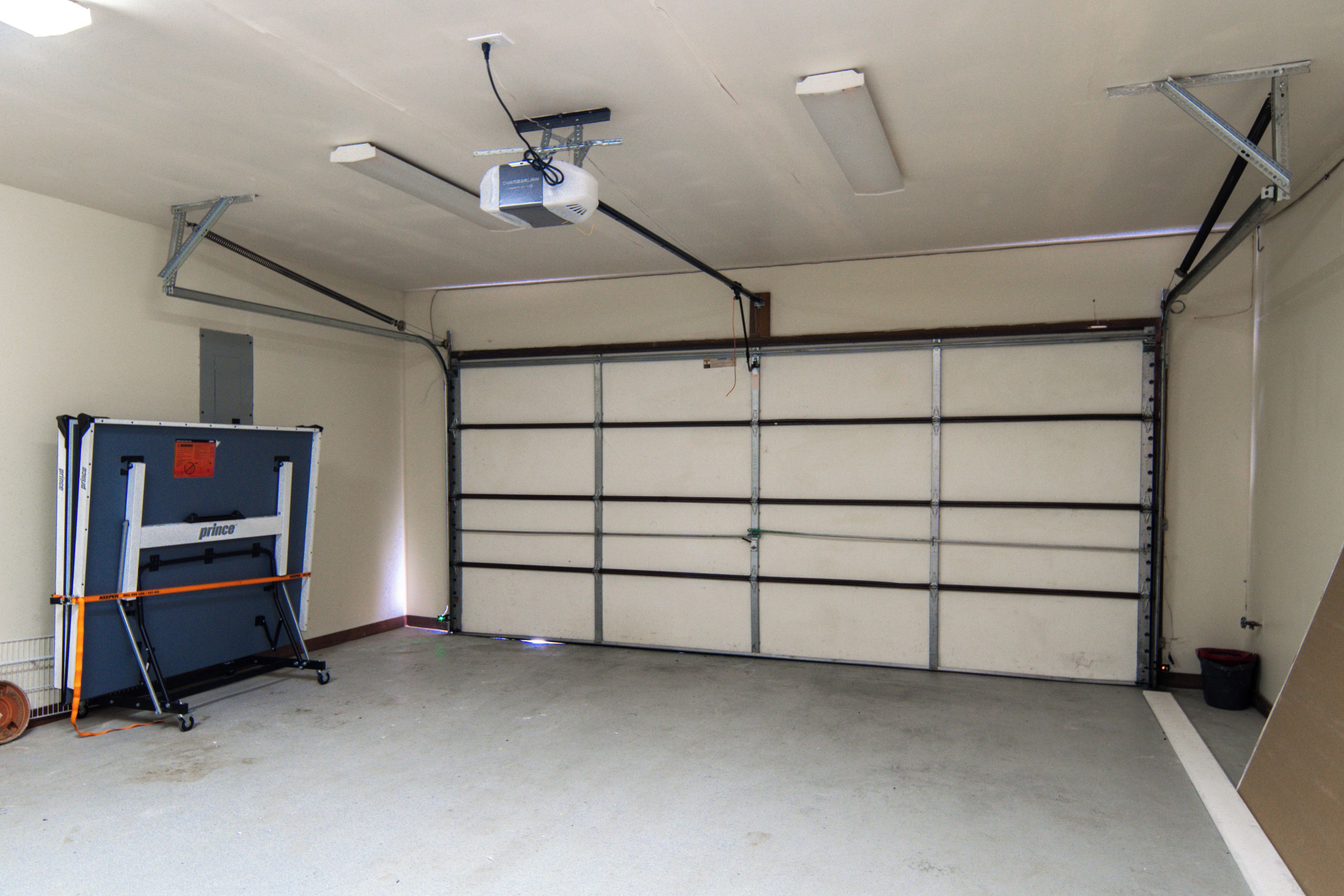 A garage with a closed garage door, a ceiling fan, and a projector mounted on the ceiling.