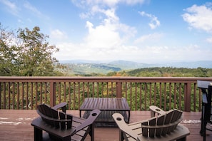 Une terrasse en bois avec deux fauteuils Adirondack et une table, offrant une vue sur un paysage montagneux.