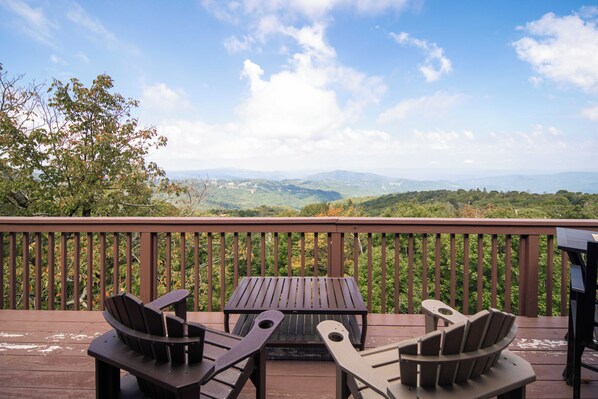 A wooden deck with two Adirondack chairs and a table, overlooking a mountainous landscape. - Pet-Friendly 5BR Home! Spectacular Mtn Views, Hot Tub, 5 min to Beech Ski (Beech Mountain)