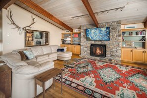 A cozy living room with a stone fireplace, a large flat-screen TV, a patterned rug, and a white leather sofa. - Pet-Friendly 5BR Home! Spectacular Mtn Views, Hot Tub, 5 min to Beech Ski (Beech Mountain)