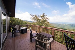 Une terrasse en bois, agréée de mobilier d’extérieur comprenant des chaises et une table, qui offre une vue panoramique sur un paysage verdoyant, avec des arbres et des collines à l’horizon.