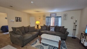 A living room with two couches, a lamp, a rug, and a 'Welcome' sign on the wall. - Cozy 3-bedroom, 2 full bath mobile home on half acre in charming Welaka! (Welaka)
