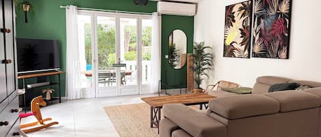 A living room with a sofa, a TV, a dining table, and a large window.