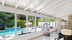 Un área de piscina interior moderna con paredes de vidrio, pared de piedra y un comedor con mesa y sillas.
