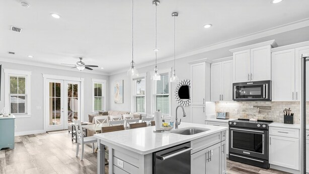 A modern kitchen with white cabinetry, a central island, stainless steel appliances, and pendant lighting.