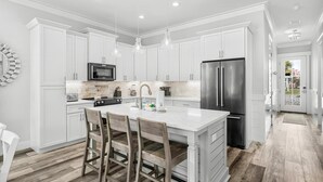 A modern kitchen with white cabinetry, stainless steel appliances, and a central island with bar stools.
