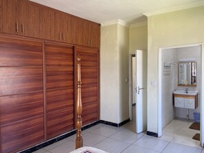 A room with wooden wardrobes, a door leading to a bathroom, and a tiled floor.