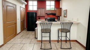 Cocina compacta con una isla central, dos taburetes de bar, un refrigerador y armarios de madera.